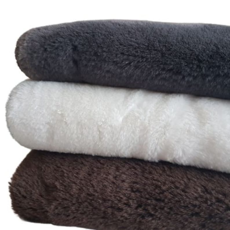 May include: Three faux fur fabric swatches in different colors: dark gray, white, and brown. The swatches are stacked on top of each other.