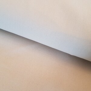 May include: Close-up of a light beige fabric with a subtle woven texture. The fabric is folded in half, showing the smooth surface on one side and the textured surface on the other.