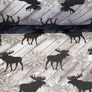 May include: A brown and white patterned fabric with a repeating pattern of black moose silhouettes and snowflakes. The fabric has a woodgrain texture.
