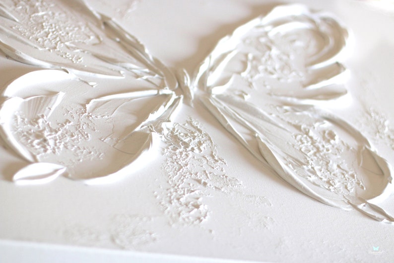 Op de afbeelding: Witte textuurverf van een vlinder op een canvas. De vlinder is geschilderd in een 3D-stijl met verhoogde verf.
