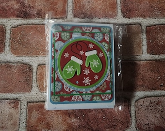 May include: A Christmas card with a red, white, and blue background featuring two green mittens with white trim and snowflakes. The mittens are tied together with a white string.
