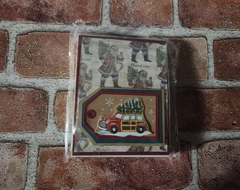 May include: A handmade Christmas card featuring a red and yellow vintage car with a Christmas tree on top. The card has a brown, gold, and green border and a pattern of Santa Claus figures on the back.