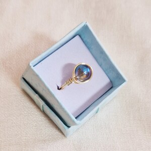 Pode incluir: Um anel de fio de ouro com uma conta de vidro azul iridescente.