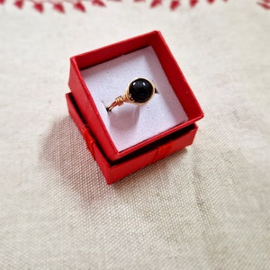May include: A black gemstone ring with a gold wire setting, displayed in a red velvet ring box.