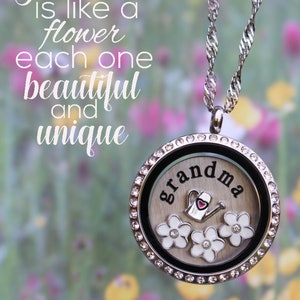 May include: A silver locket necklace with a white background and the word "grandma" in black lettering. The locket has a small red heart and three white flowers with a watering can charm inside. The background is a blurred image of a field of flowers. The text "Lockets of Love" is at the bottom of the image.