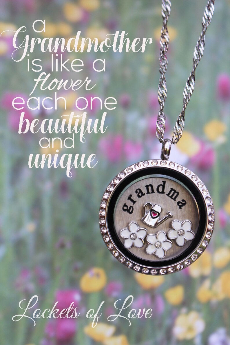 May include: A silver locket necklace with a white background and the word "grandma" in black lettering. The locket has a small red heart and three white flowers with a watering can charm inside. The background is a blurred image of a field of flowers. The text "Lockets of Love" is at the bottom of the image.
