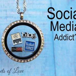 May include: A silver locket necklace with a black background and clear crystals around the edge. Inside the locket are small charms with social media icons, including a laptop, a blog, Facebook, and YouTube.