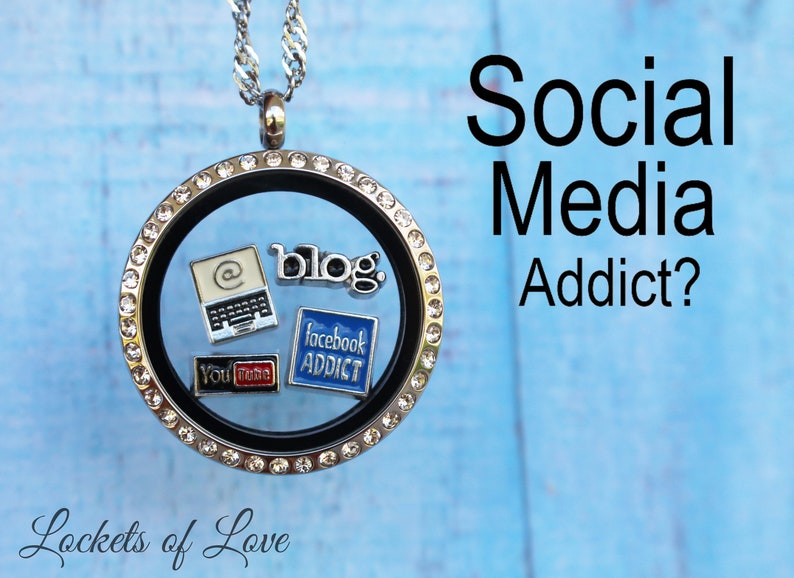 May include: A silver locket necklace with a black background and clear crystals around the edge. Inside the locket are small charms with social media icons, including a laptop, a blog, Facebook, and YouTube.