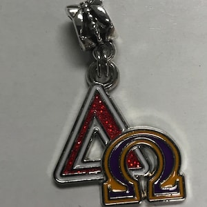 May include: A silver charm with a red triangle and a purple and gold omega symbol. The charm has a silver butterfly-shaped clasp.