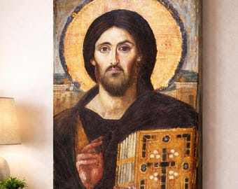 May include: A framed religious painting depicting a figure with a halo, dark hair, and a beard. The figure wears a dark robe and holds a gold book with a cross design. The painting hangs above a beige sofa with decorative pillows.