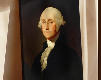 May include: A framed portrait of George Washington, featuring a black coat, white ruffled shirt, and powdered white wig. The artwork is displayed on a wooden surface, with a dark background.