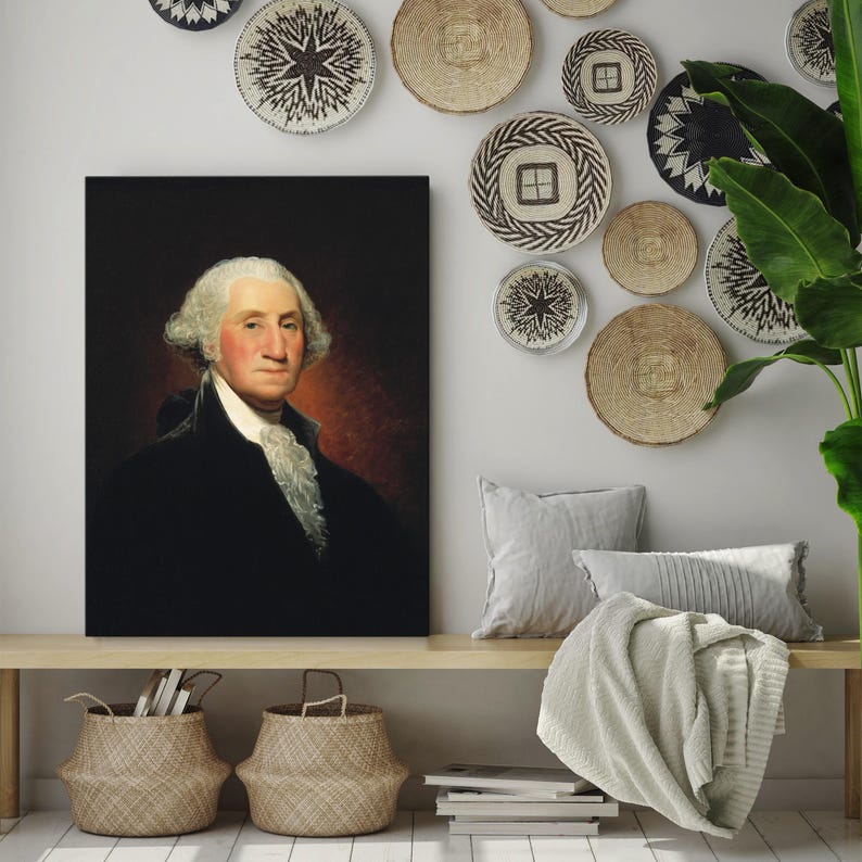 May include: A framed portrait of George Washington in a dark suit with a white cravat. The portrait is hanging on a white wall with a collection of woven wall decor.