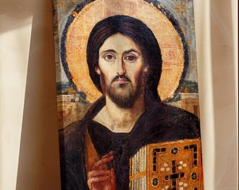 May include: A framed religious icon featuring a portrait of Jesus Christ. The artwork depicts Jesus with dark hair and a beard, set against a gold halo. He holds a book and is dressed in dark robes. The painting has a vintage, aged appearance.
