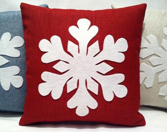 May include: Three decorative throw pillows with white felt snowflake designs. The pillows are red, blue, and beige.