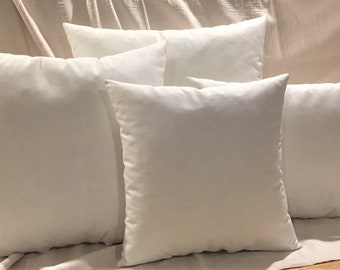 May include: Five white pillow covers arranged in a row on a white fabric surface. The pillow covers are all the same size and shape, and they are made of a soft, smooth fabric.