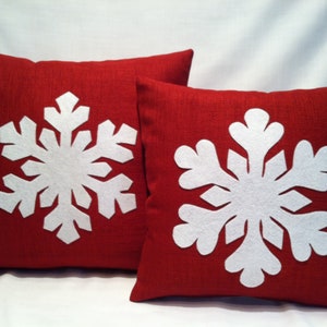 May include: Two red throw pillows with white felt snowflake designs. The snowflakes are large and detailed.