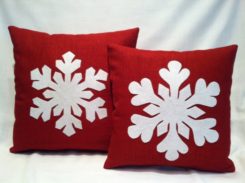 May include: Two red throw pillows with white felt snowflake designs. The snowflakes are large and detailed.