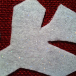 May include: White felt snowflake with glitter accents on a red background.