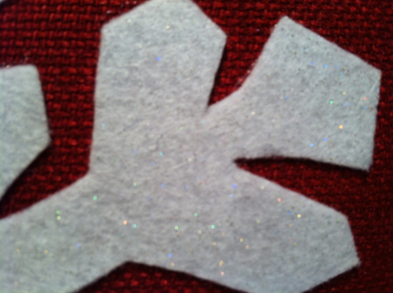 May include: White felt snowflake with glitter accents on a red background.
