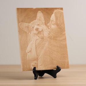 May include: A wooden plaque with a laser-engraved image of a person and a dog. The person is smiling and holding the dog in their arms. The dog is also smiling and has its tongue sticking out.