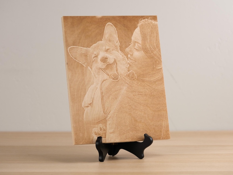 May include: A wooden plaque with a laser-engraved image of a person and a dog. The person is smiling and holding the dog in their arms. The dog is also smiling and has its tongue sticking out.