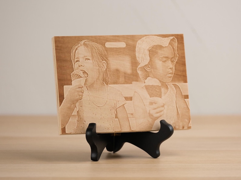 May include: A wooden plaque with a laser-engraved image of two children eating ice cream cones. The plaque is on a black stand.