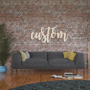 May include: A wooden sign that reads "custom" in a cursive font is mounted on a brick wall. A gray sofa with yellow and gray pillows sits below the sign. A potted plant and a patterned rug are in the foreground.