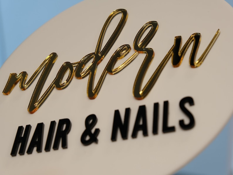 May include: A white round sign with gold lettering that says "modern" and black lettering that says "hair & nails".