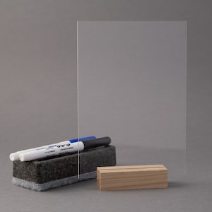 May include: A clear acrylic dry erase board with a wooden stand. Two dry erase markers and a black eraser are placed on the board.