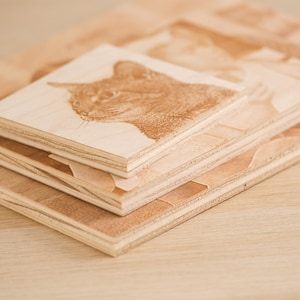 May include: Three wooden plaques stacked on top of each other. The top plaque has a laser-engraved image of a cat's head. The plaques are made of light brown wood.