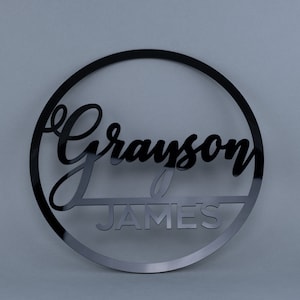 May include: Black acrylic circle with the name "Grayson James" cut out in a cursive font.