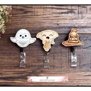 May include: Three Harry Potter themed retractable badge holders. The first features a white owl, the second a brown Dobby, and the third a brown Sorting Hat.