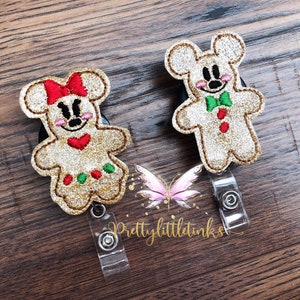 May include: Two gingerbread character badge reels with glitter accents. The characters are inspired by Mickey Mouse and Minnie Mouse. The badge reels are attached to clear plastic retractable badge holders. The text "Prettylittletinks" is visible in the image.