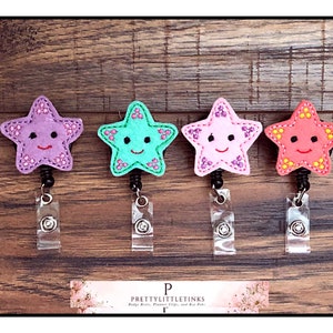 May include: Four colorful star-shaped badge reels with smiling faces. The stars are purple, teal, pink, and orange. The badge reels are on a wooden background.