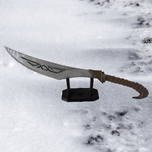 May include: A silver and brown fantasy-style dagger with a curved blade and a decorative handle. The dagger is displayed on a black stand.