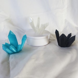 May include: Three crystal clusters in different colors: blue, white, and black. The crystals are displayed on a white circular base.