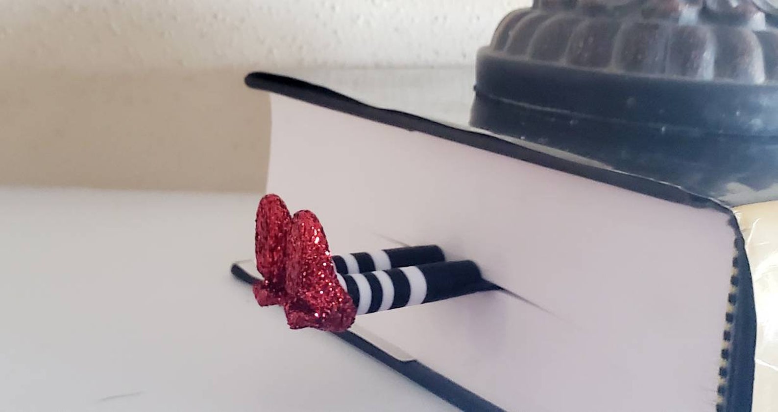 A pair of two plastic legs with striped tights and sparkly red shoes sticking out of a book.