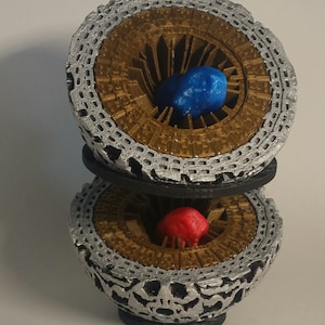 May include: A 3D printed, silver and gold, sphere-shaped object with a blue and red sphere inside. The sphere is open on the top and bottom, revealing the spheres inside.
