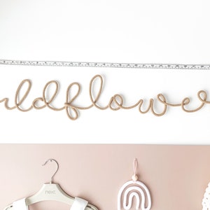 Pu&ograve; includere: Un'appendice da parete in corda beige che compone la parola "wildflower".
