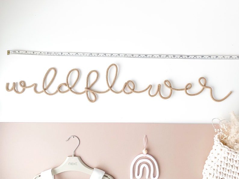 Pu&ograve; includere: Un'appendice da parete in corda beige che compone la parola "wildflower".
