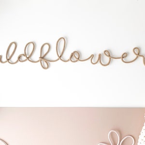 Pu&ograve; includere: Una corda di colore beige &egrave; modellata a forma della parola "wildflower" su uno sfondo bianco.