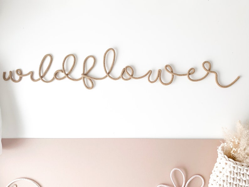 Pu&ograve; includere: Una corda di colore beige &egrave; modellata a forma della parola "wildflower" su uno sfondo bianco.