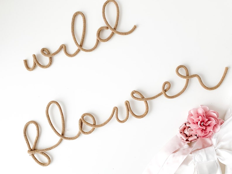Pu&ograve; includere: Uno sfondo bianco con le parole "wild flower" scritte in corda marrone. Un fiore rosa si trova nell'angolo in basso a destra dell'immagine.