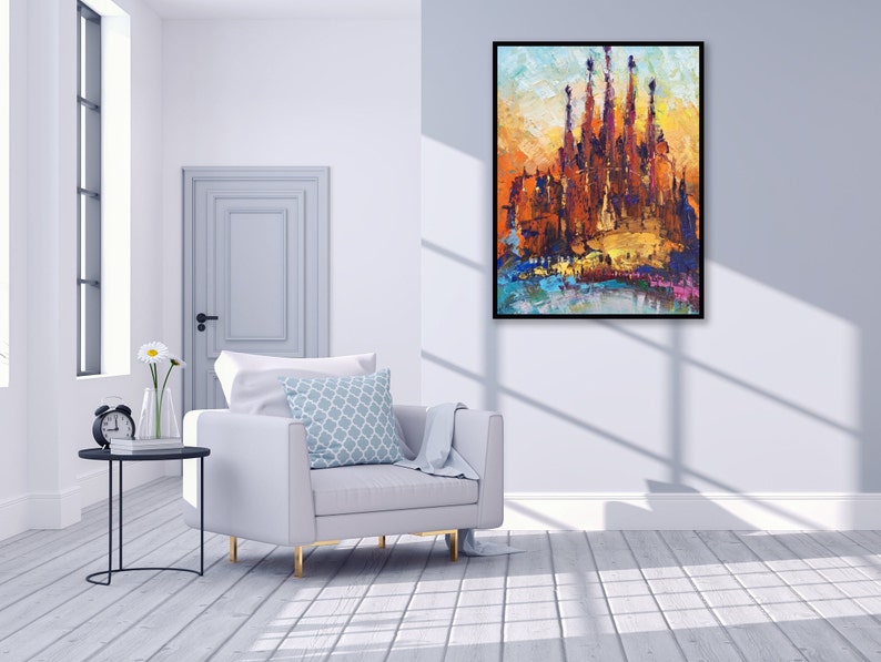 May include: A painting depicting a colourful cityscape with a large building at its centre. The building has numerous towers and is painted in shades of orange, yellow, and brown. The sky is a bright blue with clouds. The painting is framed in black.