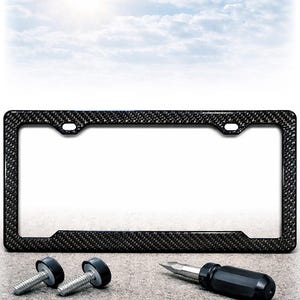 May include: A black carbon fiber license plate frame with mounting hardware and a screwdriver. The frame has a textured pattern and is designed to fit a standard U.S. license plate. The background is a cloudy sky.