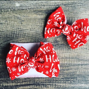 May include: Two red Christmas headbands with white snowflakes and the text "Ho Ho Ho" printed on them. The headbands are tied in a bow.