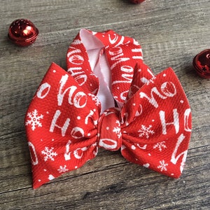 May include: Red Christmas headband with a white bow and the words "Ho Ho Ho" printed on it. The headband is decorated with white snowflakes.