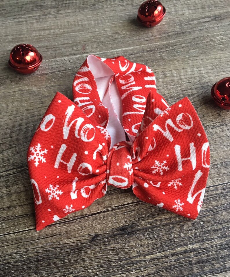 May include: Red Christmas headband with a white bow and the words "Ho Ho Ho" printed on it. The headband is decorated with white snowflakes.