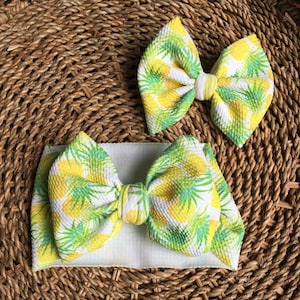 May include: Two yellow and green pineapple print fabric headbands. The larger headband is a bow and the smaller headband is a knotted headband.