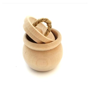 May include: A small wooden pot with a lid and a woven rope handle. The lid is slightly ajar, revealing the interior of the pot.